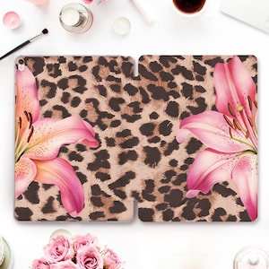 May include: A tablet case featuring a leopard print design with pink and orange lilies. The case is open, displaying the interior and exterior design. The background is a light pink color.