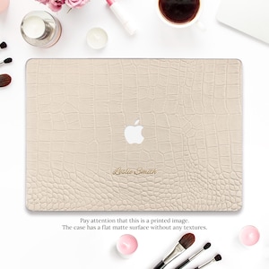 May include: A beige laptop case with a faux crocodile skin pattern. The Apple logo is visible, along with the name "Leslie Smith" in gold script. The text at the bottom reads "Pay attention that this is a printed image. The case has a flat matte surface without any textures."