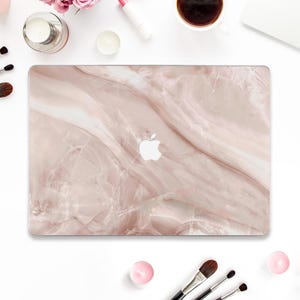 May include: A pink and white marble laptop skin with a white Apple logo in the centre.