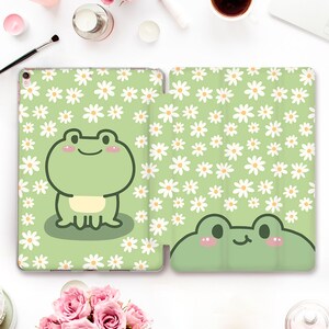 May include: A green tablet case with a white daisy pattern and a cartoon frog design. The case is closed and the frog is smiling.