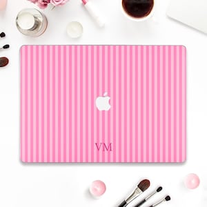 May include: Pink and light pink striped laptop case with the Apple logo and the initials "VM". The case is on a white surface with makeup brushes, candles, and a cup of coffee.