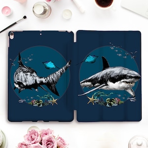 May include: Navy blue iPad case featuring a detailed illustration of two sharks in a marine environment. The sharks are depicted in black and white, set against a dark blue background with a circular design. The case includes images of stingrays, coral, and starfish.