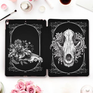 May include: A black and white illustration of two animal skulls with floral accents. The skulls are surrounded by ornate frames. The background is black.
