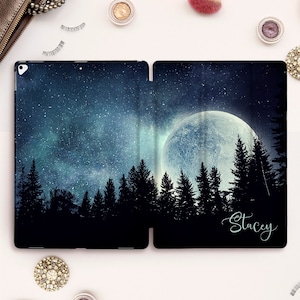 Può includere: Una custodia nera per iPad con un design a luna piena e silhouette di bosco. La custodia ha uno sfondo di cielo stellato e il nome "Stacey" è scritto in corsivo bianco sul lato destro.