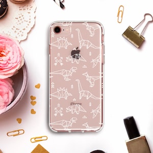 Può includere: Una custodia per telefono trasparente con un motivo di dinosauro geometrico bianco. La custodia ha la scritta "iPhone" stampata sul retro.