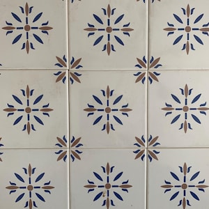 May include: Nine white ceramic tiles with a repeating pattern of blue and brown stylized floral designs. The tiles are arranged in a 3x3 grid.