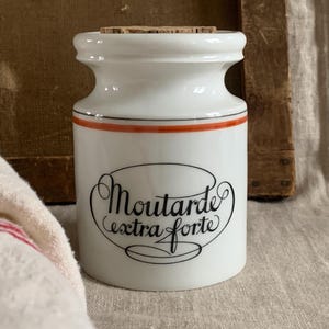 Puede incluir: Tarro de cerámica blanco con tapa de corcho y una etiqueta roja y negra que dice "Moutarde extra forte".