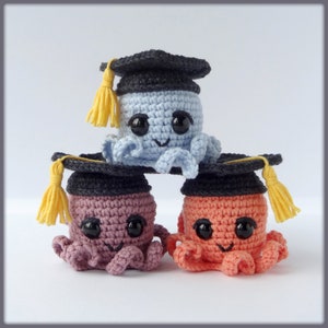Puede incluir: Tres peluches de pulpo de crochet con gorros de graduación. El pulpo de arriba es azul claro, el pulpo del medio es rosa y el pulpo de abajo es naranja.