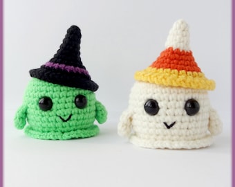 Könnte beinhalten: Zwei gehäkelte Halloween-Figuren. Eine ist grün mit einem schwarzen Hexenhut mit lila Band. Die andere ist weiß mit einem Candy-Corn-Hut. Beide haben schwarze Augen und lächelnde Münder. Die Figuren sind handgefertigt.