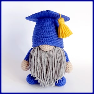 May include: A blue crocheted gnome wearing a graduation cap with a yellow tassel. The gnome has a long gray beard and is sitting with its legs crossed.
