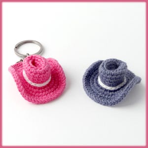 May include: Two crocheted cowboy hats, one pink and one gray, attached to a silver key ring.
