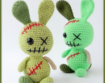 Könnte beinhalten: Zwei handgefertigte Zombie-Hasen-Puppen aus Häkelarbeit. Die Hasen sind hauptsächlich grün mit roten Nähten, schwarzen Augen und genähten Mäulern. Ein Hase ist hellgrün, der andere ist dunkler grün. Die Ohren sind aufrecht und die Arme und Beine sind klein.