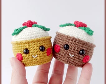 May include: Two crocheted, smiling food-themed amigurumi. One is yellow, the other brown, both with white tops, red accents, and green leaves. They have black eyes and red cheeks. The amigurumi are held in a person's hand.