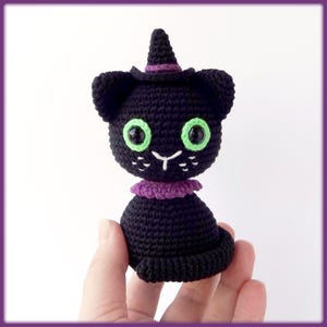 May include: Black crocheted cat wearing a purple witch hat with green eyes.
