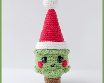 Könnte beinhalten: Gehäkelter Weihnachtsbaumschmuck mit einem lächelnden Gesicht, roter Wangen und einem braunen Sockel. Der grüne Baum trägt einen rot-weißen Weihnachtsmütze, hat schwarze Augen und eine weiße Bommel oben.