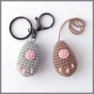 May include: Two crocheted paw print keychains, one gray and one brown, with pink accents. The gray keychain is attached to a silver key ring, while the brown keychain has a brown string loop.