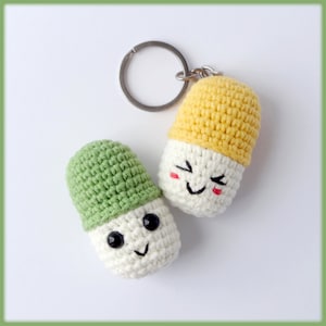 May include: Two crocheted pill-shaped keychains with smiling faces. One keychain is green and the other is yellow.