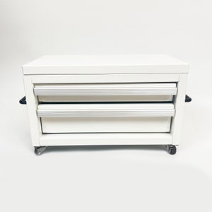 May include: White metal rolling tool chest with two drawers. The chest has black handles and wheels.