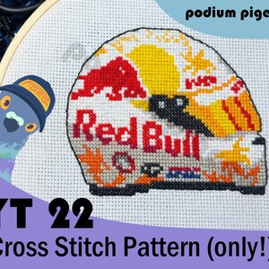 Może przedstawiać: Wzór do haftu krzyżykowego na białej tkaninie przedstawiający kask wyścigowy w kolorach czerwonym, żółtym i białym, logo Red Bull oraz tekst. Po lewej stronie znajduje się rysunkowy gołąb w czapce z napisem podium pigeon oraz YT 22 Cross Stitch Pattern.
