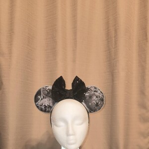 May include: Black and white mouse ears with a black bow. The ears have a spiderweb pattern.