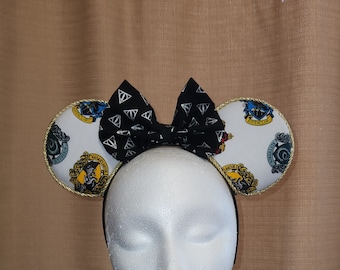 May include: A pair of black and white themed mouse ears with a black bow featuring white lightning bolts. The ears are white with gold trim and feature the crests of the Hogwarts houses. A fun accessory for fans.