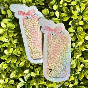Pode incluir: Dois adesivos em forma de jarra com um design floral e a palavra "Mama" em rosa. Cada adesivo tem um la&ccedil;o rosa no topo. Um adesivo tem o n&uacute;mero "7" na parte inferior. O fundo &eacute; uma cama de folhas verdes.