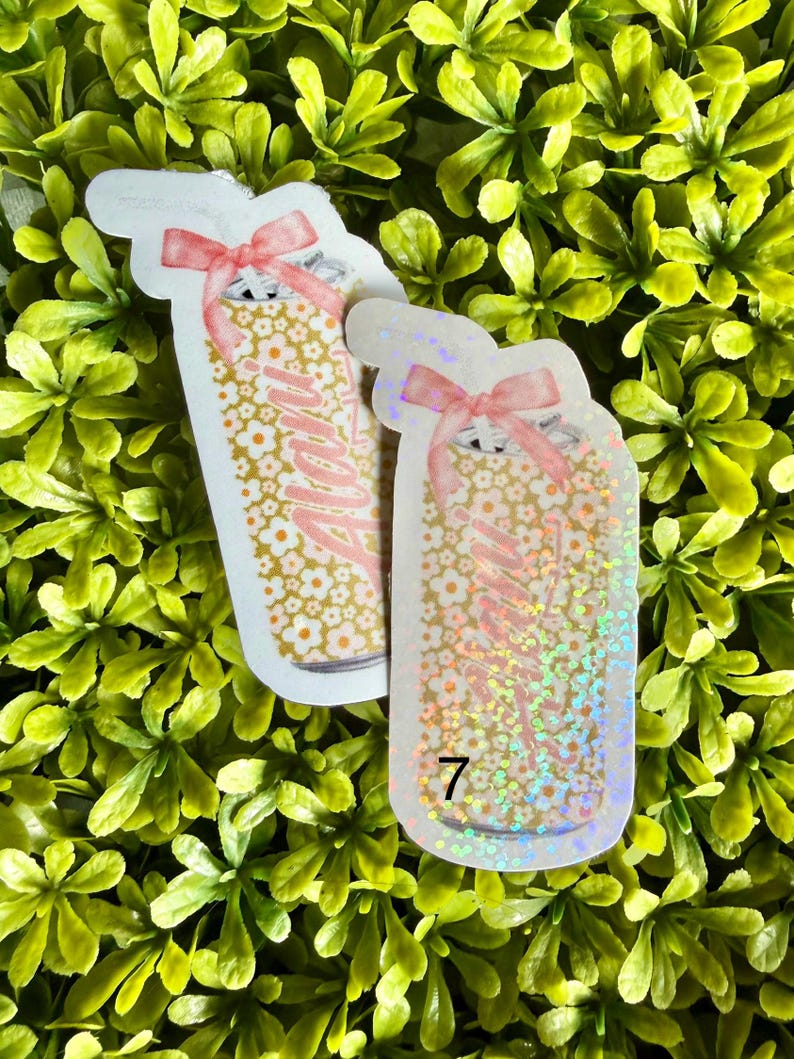 Pode incluir: Dois adesivos em forma de jarra com um design floral e a palavra "Mama" em rosa. Cada adesivo tem um la&ccedil;o rosa no topo. Um adesivo tem o n&uacute;mero "7" na parte inferior. O fundo &eacute; uma cama de folhas verdes.