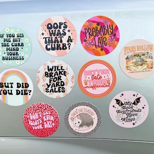 May include: A collection of ten circular stickers featuring various designs and text including If You See Me Hit The Curb Mind Your Business, Oops Was That A Curb, Probably Late, Stars Hollow, But Did You Die, Will Brake For Yard Sales, Better Late Than Uncaffeinated, Don't Let Idiots Ruin Your Day, Cute But Trashy with an opossum, and My Book Boyfriends Have Wings.