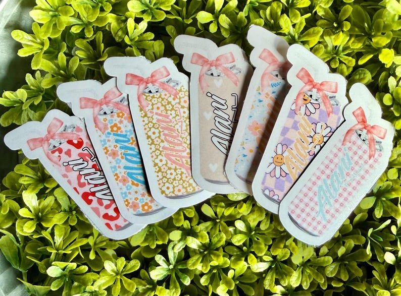 Pode incluir: Uma cole&ccedil;&atilde;o de autocolantes coloridos com um design de frasco, cada um adornado com um la&ccedil;o rosa e o nome "Alani". Os autocolantes apresentam v&aacute;rios padr&otilde;es, incluindo florais, cora&ccedil;&otilde;es e xadrez, num fundo de folhagem verde.