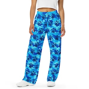 May include: Blue patterned pants with a paw print design. The pants have a wide leg cut and a blue camouflage pattern. The paw prints are a darker shade of blue. The model is wearing a white crop top.