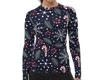 May include: A long-sleeve crew neck shirt featuring a dark navy blue background with a repeating holiday pattern. The print includes white snowflakes, green pine needles, red berries, and red and white striped candy canes throughout.