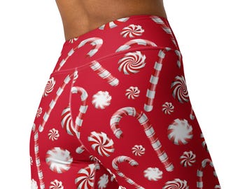 May include: High-waisted leggings featuring a vibrant red background with a repeating pattern of white and red striped candy canes and round peppermint swirl candies. The garment has a fitted silhouette and a wide waistband for a secure fit.