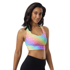May include: A colorful sports bra with a halter neckline. The bra features a vibrant pattern of pastel stars in shades of pink, yellow, blue, and green. The model is wearing black leggings. The overall theme is activewear.