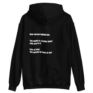Op de afbeelding: Zwart hoodie met een witte boodschap op de rug die luidt: "Lieve persoon achter me, De wereld is een betere plek met jou erin. Veel liefde, De persoon voor je."