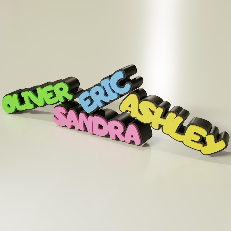 Puede incluir: Cuatro letreros con nombres en 3D con una fuente l&uacute;dica. Los nombres son "Oliver" en verde, "Eric" en azul, "Sandra" en rosa y "Ashley" en amarillo. Cada nombre est&aacute; sobre un fondo negro.