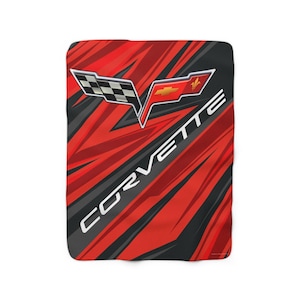May include: A red, black, and white Corvette-themed blanket. The blanket features the Corvette logo and the word "CORVETTE" in white. The background has a red and black abstract design.