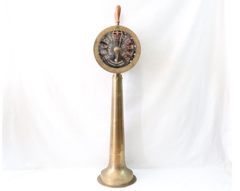 May include: A vintage brass ship's telegraph with a wooden handle. The circular dial displays speed commands like "FULL" and "SLOW" in black lettering. The telegraph stands on a flared base and is a classic nautical item.