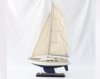 May include: A white model sailboat with a blue hull and a wooden base. The sails are made of fabric and are raised.