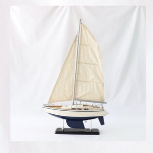 May include: A white sailboat model with a blue hull and a wooden base. The sails are made of fabric and are raised.