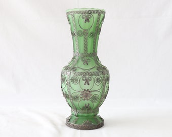 May include: A green glass vase with silver filigree detailing. The vase has a round body and a narrow neck.
