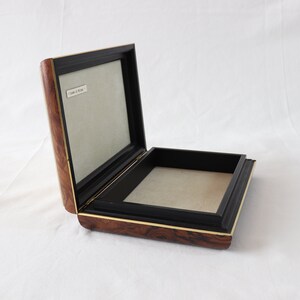 May include: A wooden box with a black interior and a gold trim. The box is open and the inside is lined with a light brown fabric.