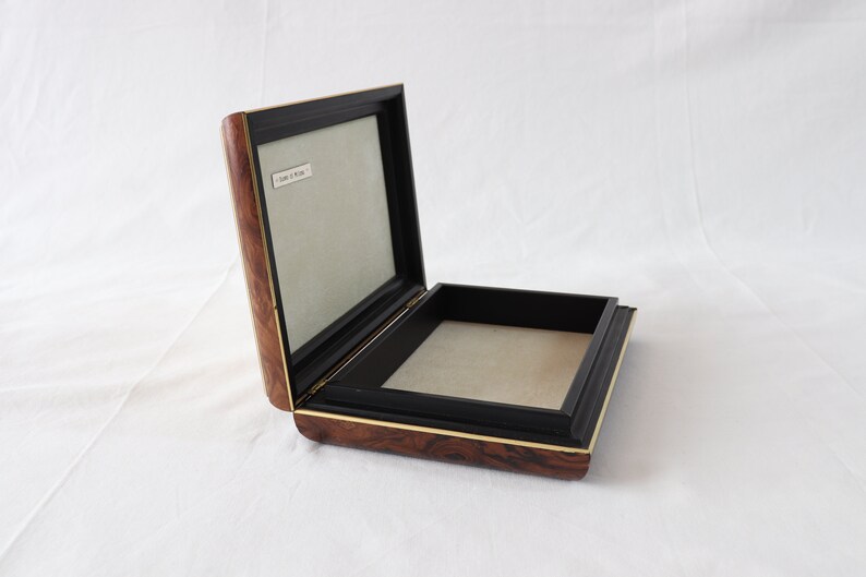 May include: A wooden box with a black interior and a gold trim. The box is open and the inside is lined with a light brown fabric.