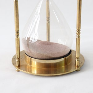 May include: A brass hourglass with a clear glass bulb and a round base. The sand is a light brown color.