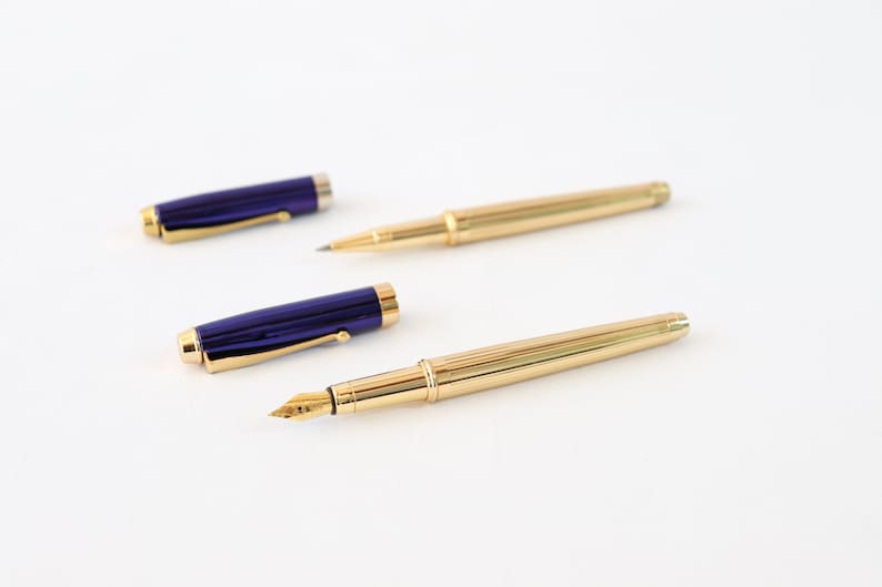 May include: Two pens, one with a gold barrel and a blue cap, and the other with a gold barrel and a gold cap.