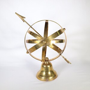 May include: A gold-toned metal armillary sphere with a compass needle on a bell-shaped base.