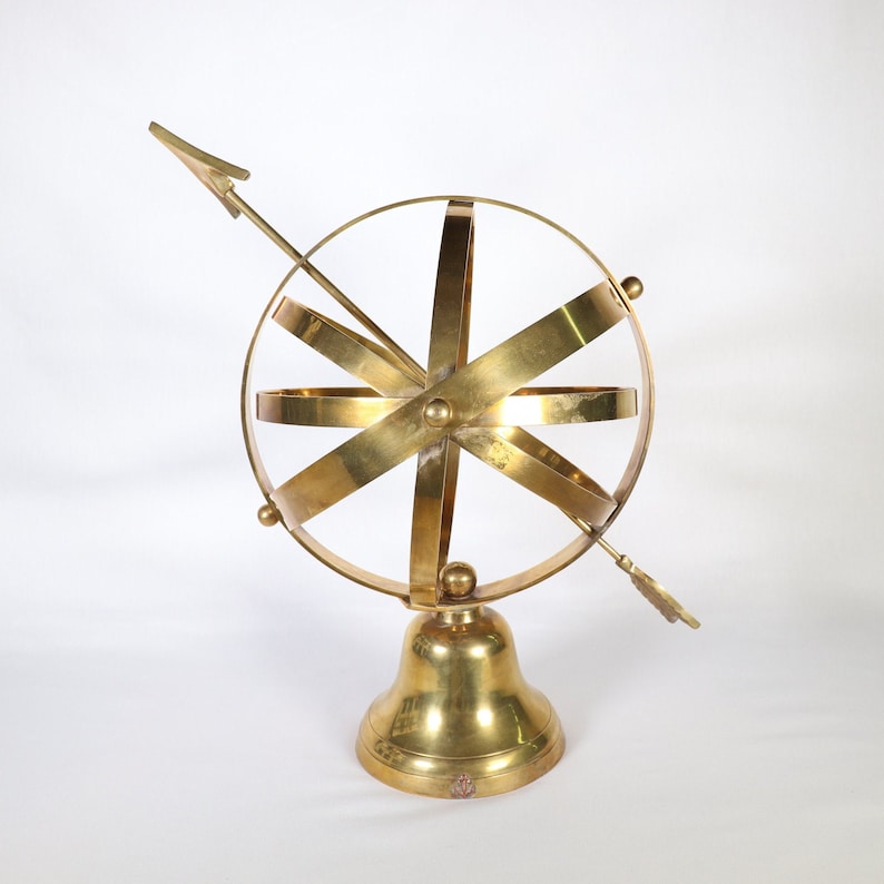 May include: A gold-toned metal armillary sphere with a compass needle on a bell-shaped base.