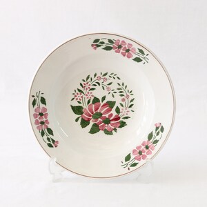 May include: White ceramic soup bowl with a floral design featuring pink and green flowers. The bowl has a gold rim.