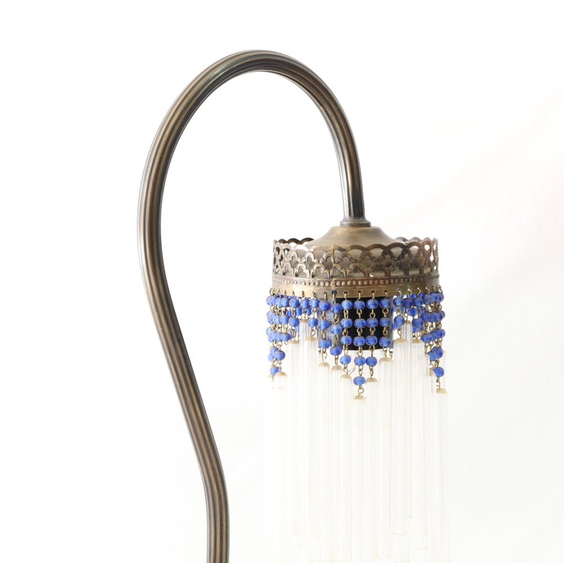 K&ouml;nnte beinhalten: Eine Stehlampe aus Messing mit einem gebogenen Arm und einem dekorativen Schirm. Der Schirm ist mit blauen Perlen und durchsichtigen Glasf&auml;den verziert.