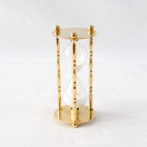 Pu&ograve; includere: Una clessidra color oro con un centro in vetro trasparente riempito di sabbia bianca. La clessidra ha una base e una parte superiore circolari, con tre supporti decorativi. Il design generale &egrave; simmetrico ed elegante.