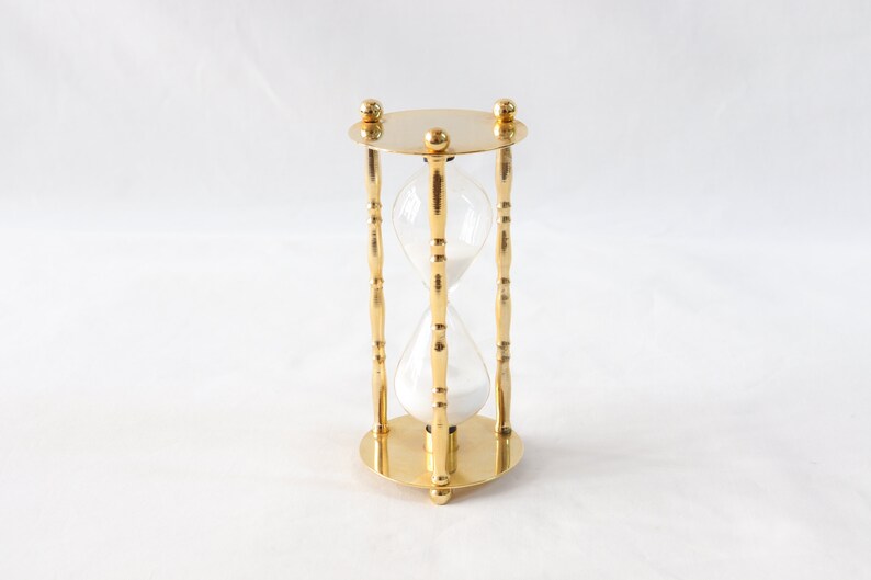Pu&ograve; includere: Una clessidra color oro con un centro in vetro trasparente riempito di sabbia bianca. La clessidra ha una base e una parte superiore circolari, con tre supporti decorativi. Il design generale &egrave; simmetrico ed elegante.